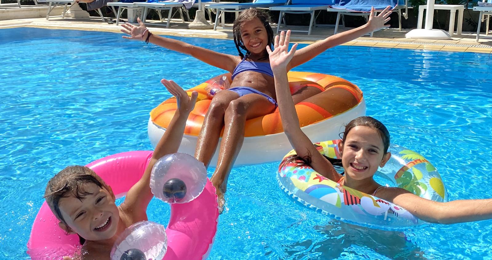 Persone saltano in piscina sotto un ombrellone Motta in una giornata di sole.