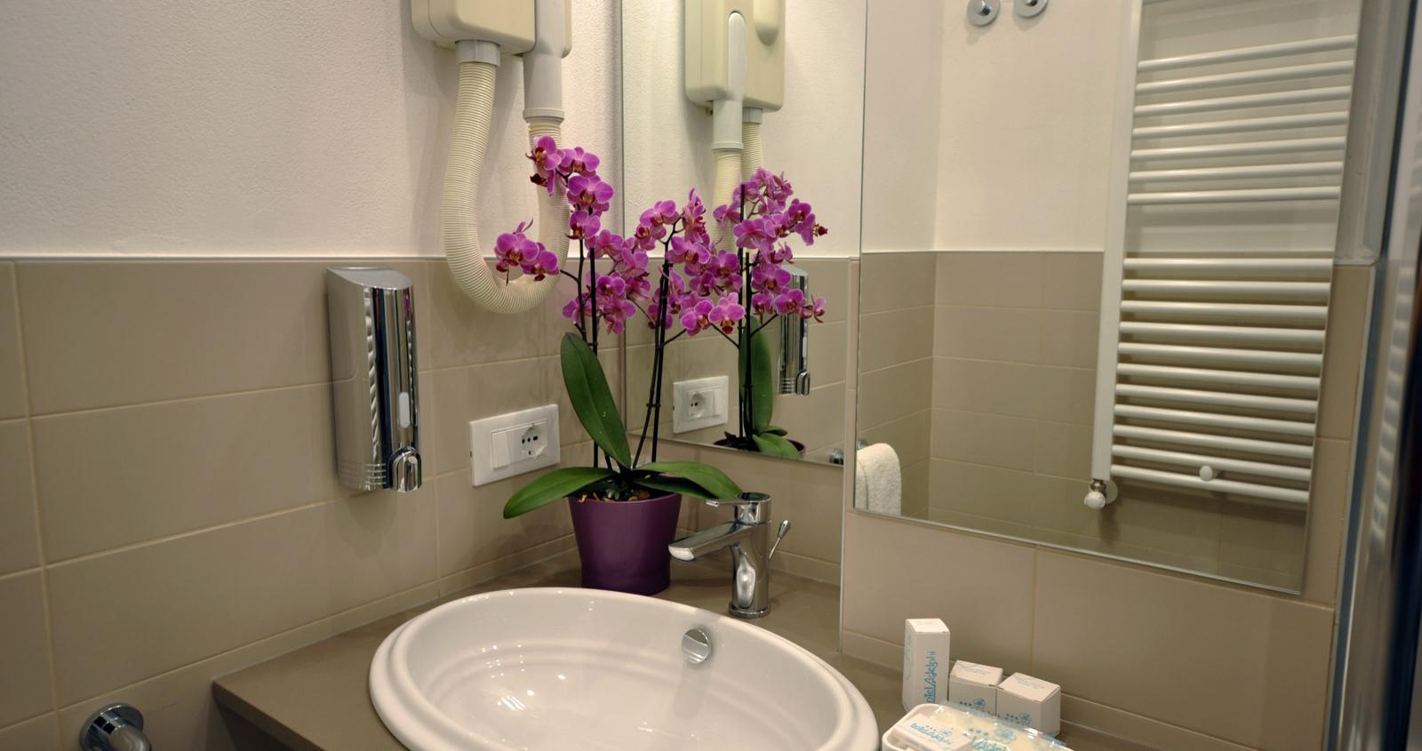 Bagno moderno con lavabo, specchio, fiori viola e accessori da toeletta.