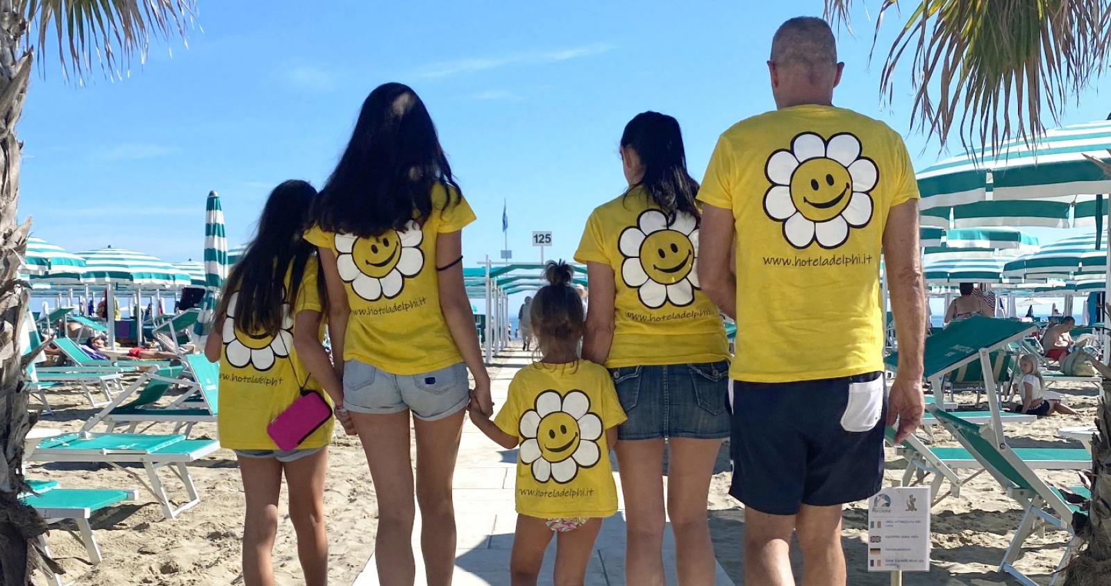 Famiglia in spiaggia con magliette gialle e logo di un fiore sorridente.