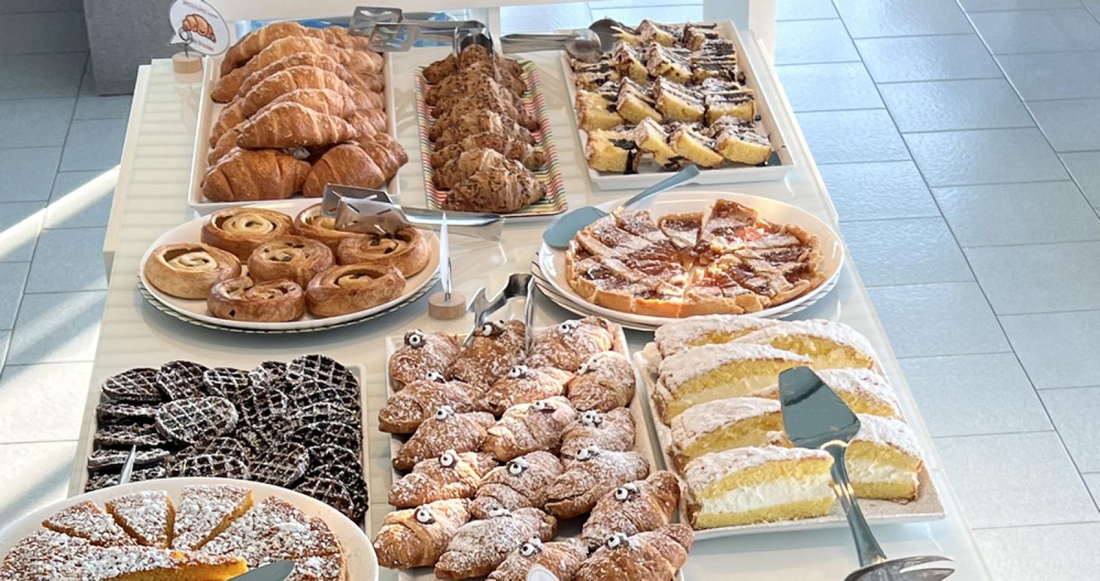 Buffet con dolci assortiti: torte, croissant, ciambelle e biscotti su tavolo bianco.