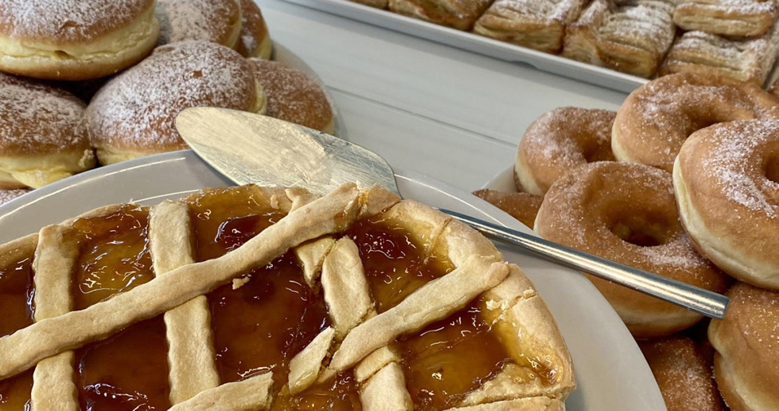 Dolci vari: crostata, bomboloni, ciambelle e sfogliatine su un tavolo.