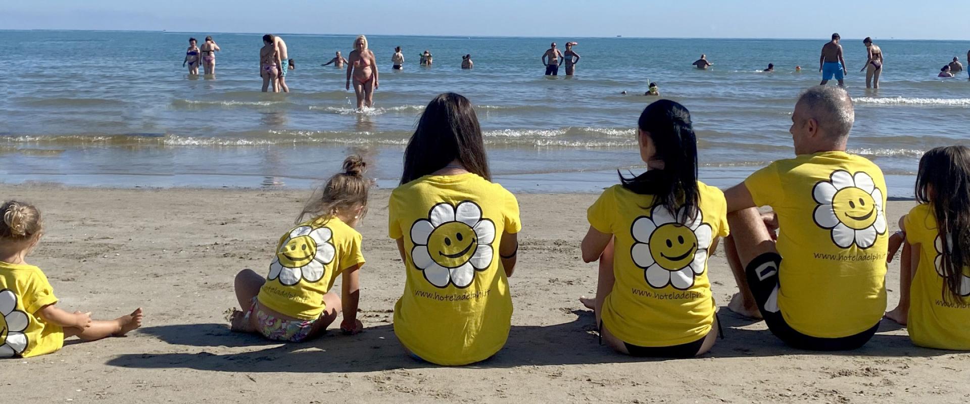 Famiglia in magliette gialle con fiore sorridente seduta sulla spiaggia.