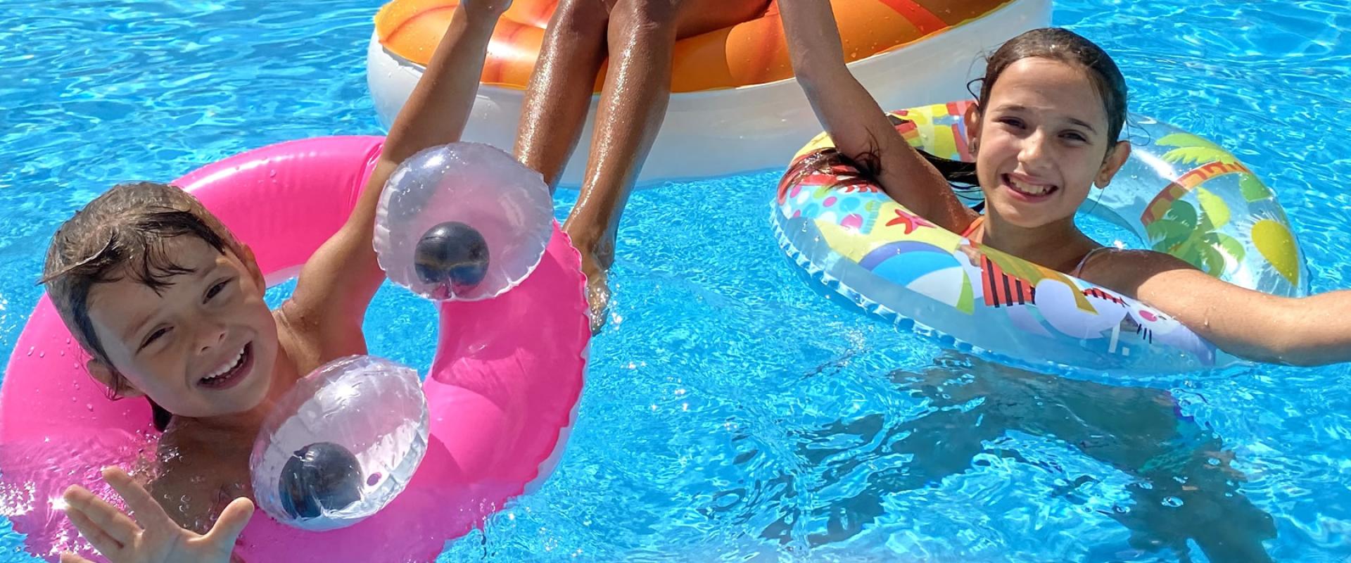 Bambini si divertono in piscina, spruzzando acqua e ridendo sotto il sole.