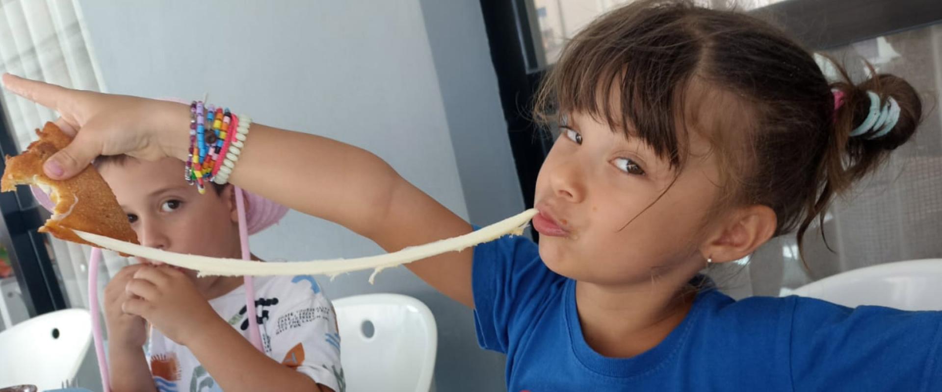 Bambina con treccine mangia un panino con formaggio filante, indossa braccialetti colorati.