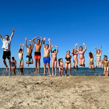 Gruppo di persone sorridenti in cerchio, indossano magliette blu con una lettera gialla.