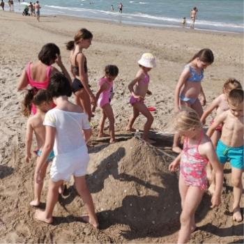 Bambini giocano sulla spiaggia intorno a un castello di sabbia.