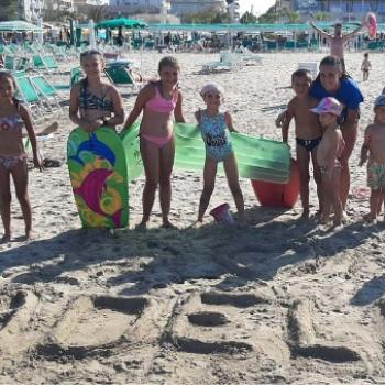 Bambini in spiaggia con tavole da surf e scritta sulla sabbia.