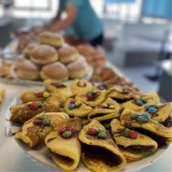 Pancakes ripieni di cioccolato con caramelle colorate, ciambelle sullo sfondo.