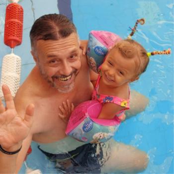 Uomo e bambina sorridenti in piscina, con braccioli colorati e acconciatura divertente.