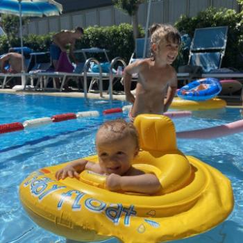 Bambini in piscina, uno su un gonfiabile giallo, l'altro sorride in piedi.