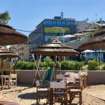 Spiaggia con ombrelloni di paglia e sedie, edificio moderno sullo sfondo.