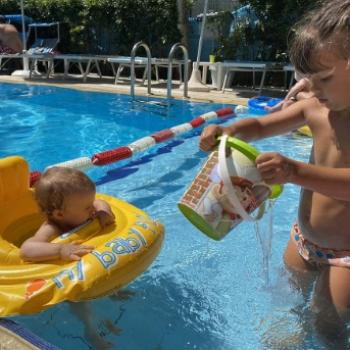 Kids playing in a pool with a float and a bucket.