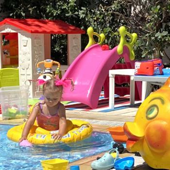 Piscina affollata con ombrelloni blu e persone che si rilassano al sole.